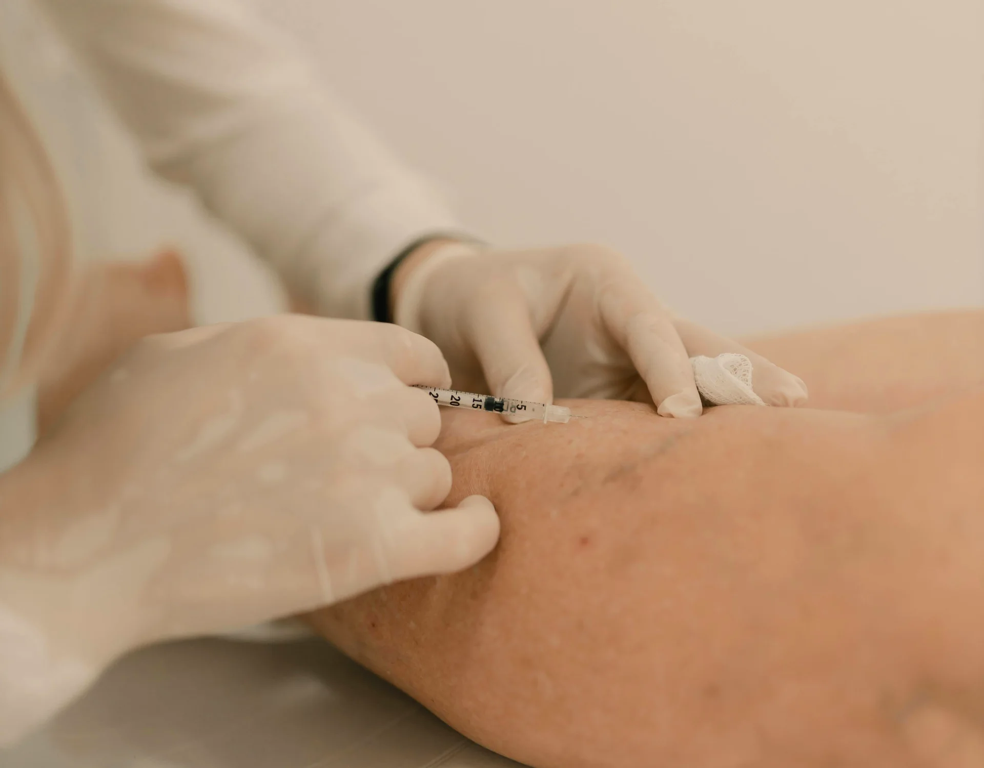 Nurse or clinician wearing gloves administers a syringe injection into a patient’s upper arm, with a small bandage nearby.